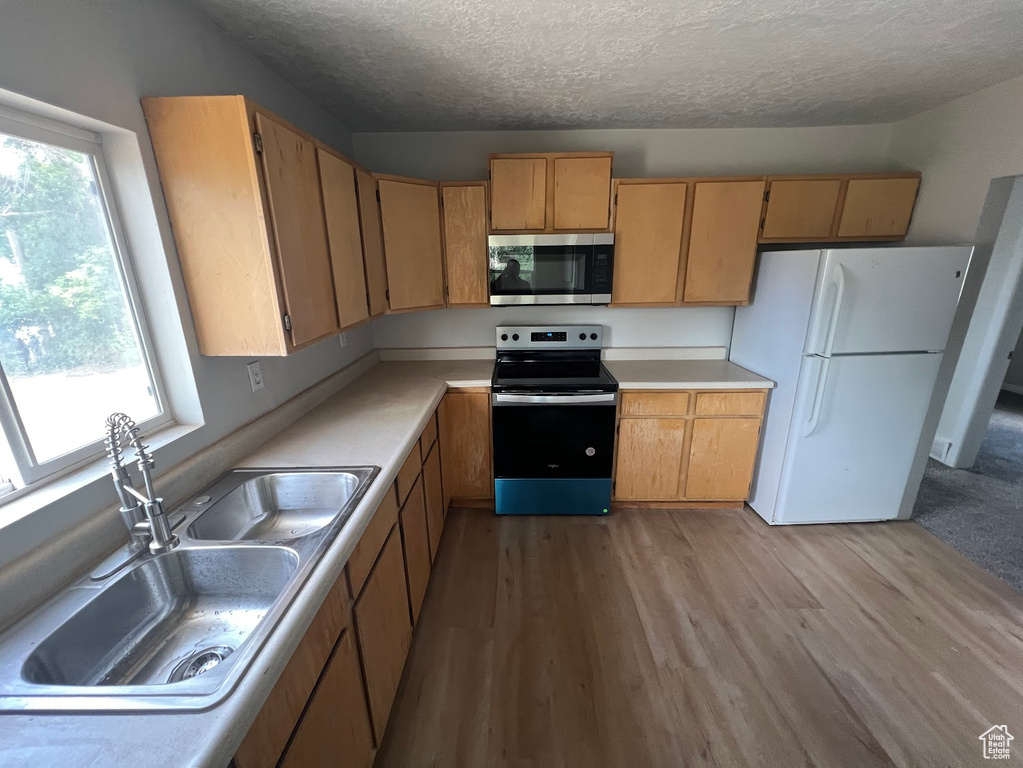 Kitchen featuring stainless steel microwave, range with electric cooktop, freestanding refrigerator, a textured ceiling, and wood finished floors