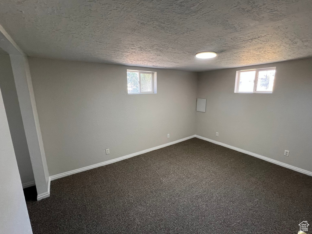 Below grade area featuring a textured ceiling, healthy amount of natural light, and dark carpet