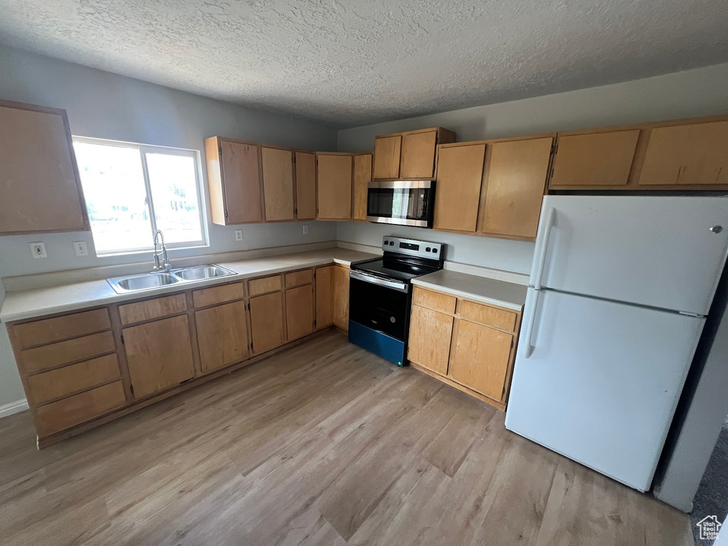Kitchen with electric range, freestanding refrigerator, stainless steel microwave, a textured ceiling, and light wood finished floors