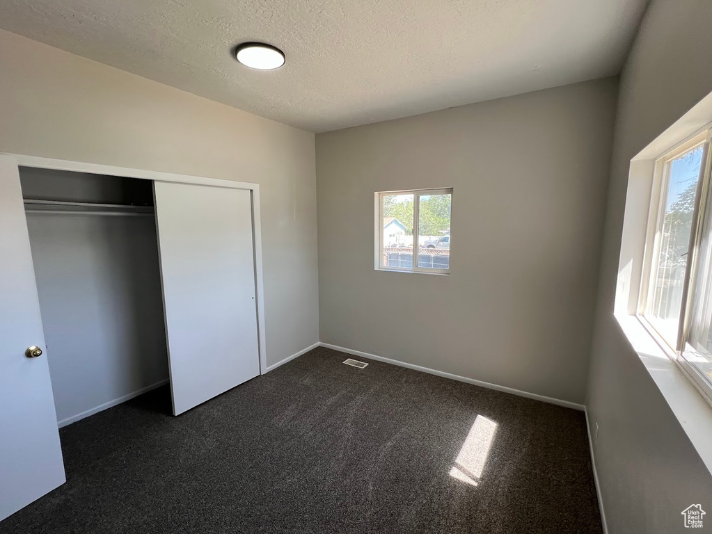 Unfurnished bedroom featuring dark colored carpet, a textured ceiling, and a closet