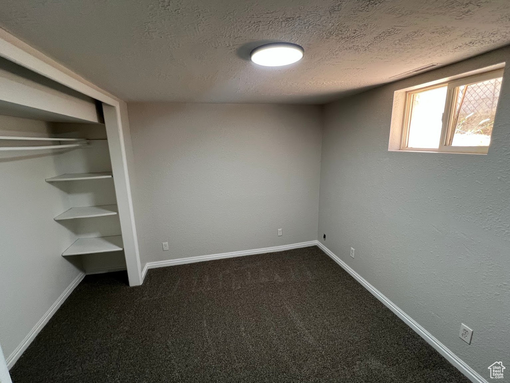 Unfurnished bedroom with a textured ceiling, dark carpet, and a closet