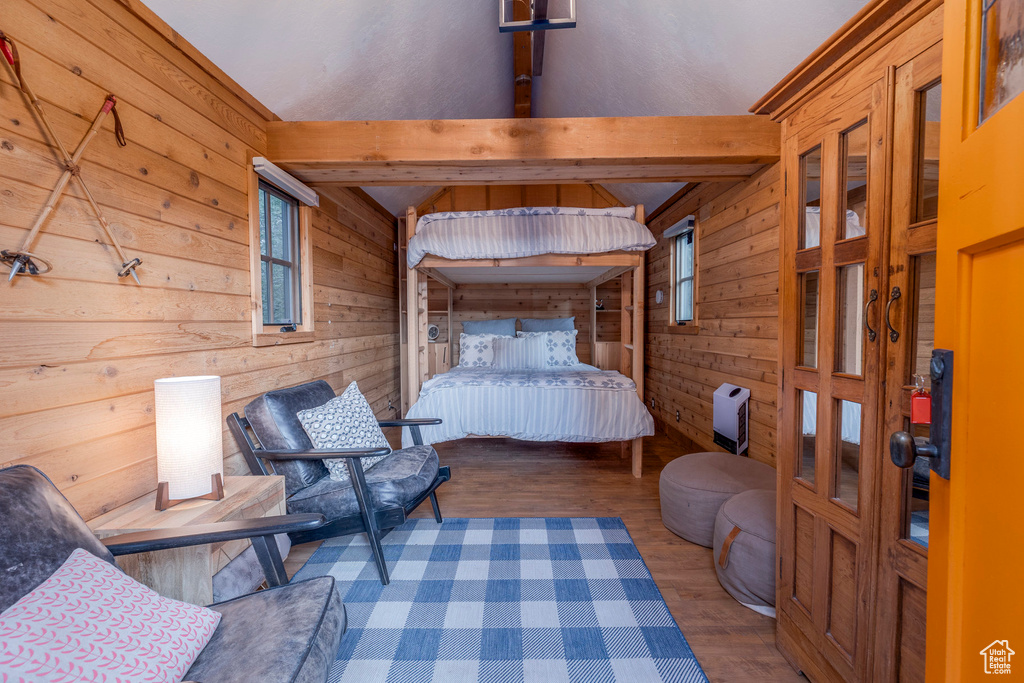 Bedroom with wooden walls, wood finished floors, and beamed ceiling