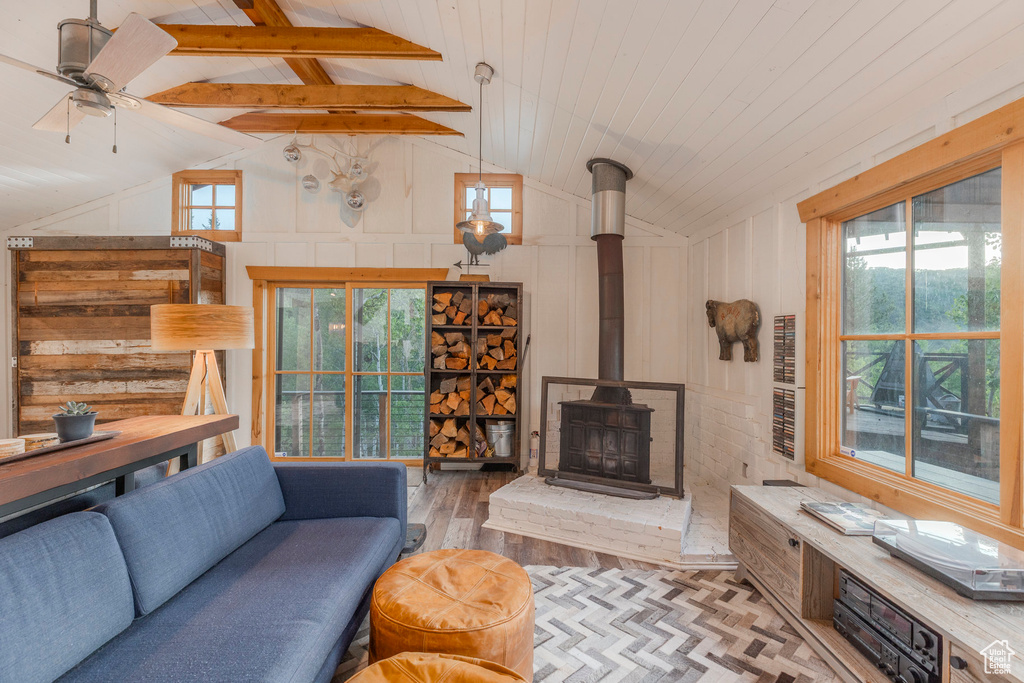 Living area featuring wood finished floors, a wood stove, high vaulted ceiling, a ceiling fan, and beamed ceiling