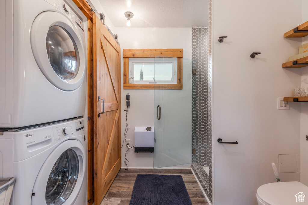 Laundry area featuring stacked washer / dryer, wood finished floors, and a barn door