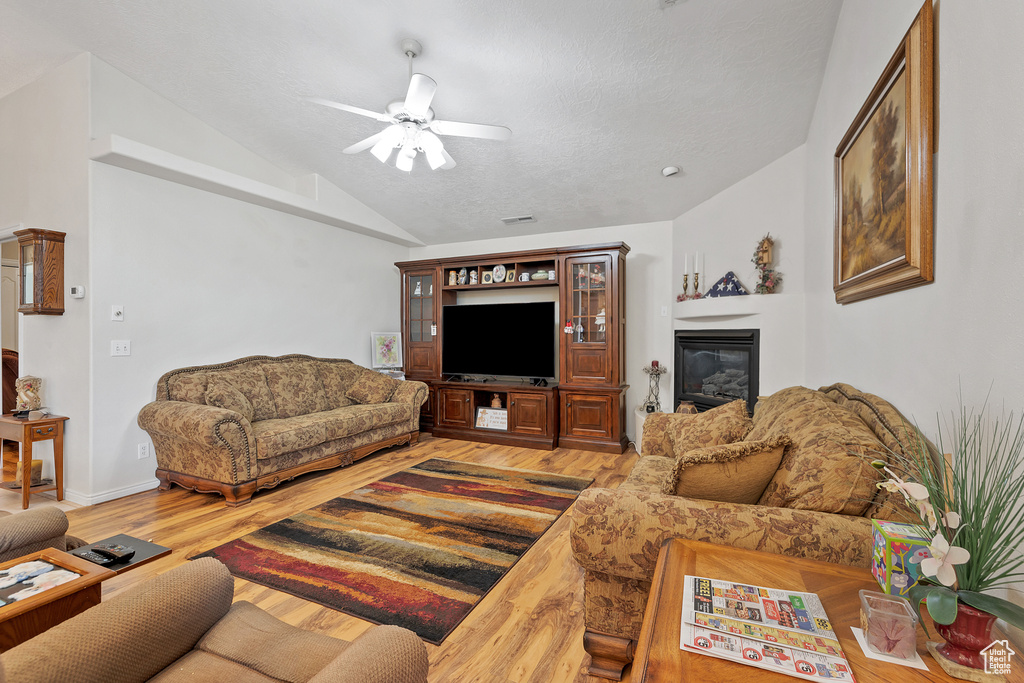 Living area with vaulted ceiling, ceiling fan, wood finished floors, and a glass covered fireplace