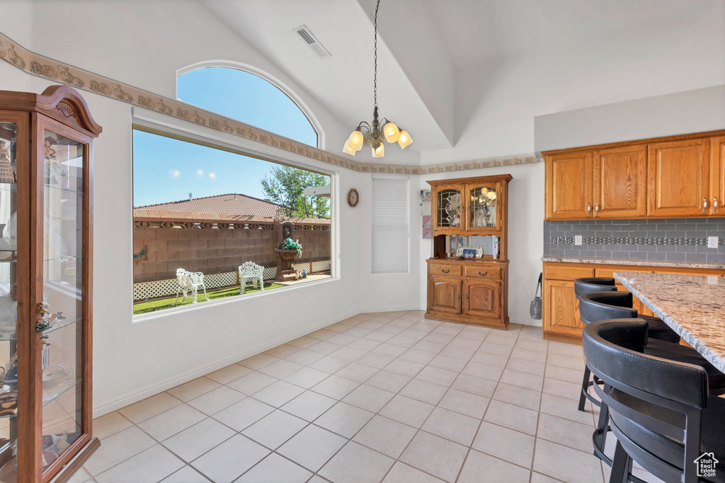 Kitchen with light tile patterned flooring, backsplash, brown cabinets, pendant lighting, and a chandelier
