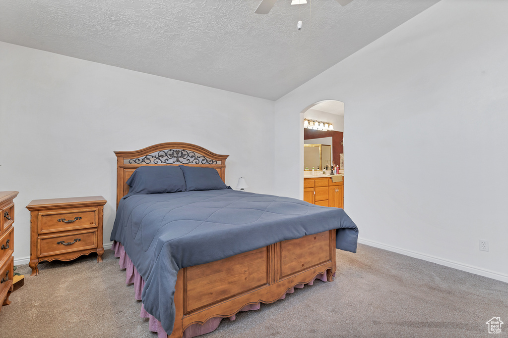 Bedroom with arched walkways, light colored carpet, a textured ceiling, ensuite bath, and ceiling fan