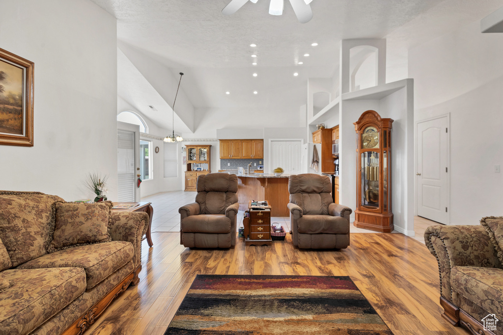Living room featuring high vaulted ceiling, ceiling fan, light wood finished floors, recessed lighting, and a chandelier