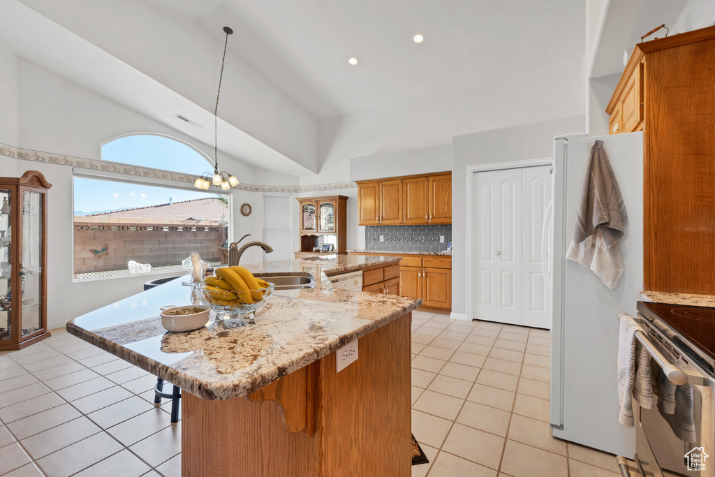 Kitchen featuring white appliances, light tile patterned floors, a breakfast bar, brown cabinetry, and tasteful backsplash