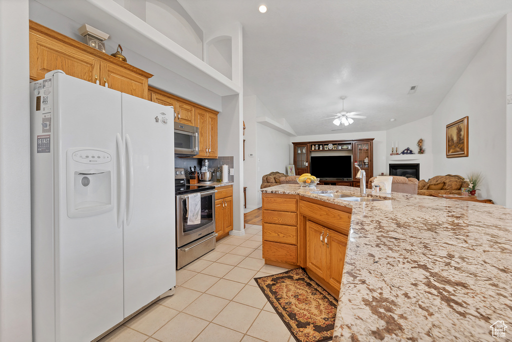 Kitchen with stainless steel appliances, a glass covered fireplace, ceiling fan, open floor plan, and vaulted ceiling