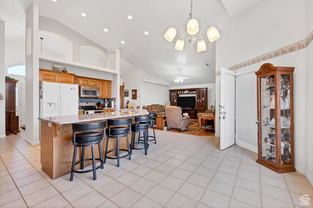 Kitchen featuring appliances with stainless steel finishes, high vaulted ceiling, a breakfast bar area, light tile patterned flooring, and open floor plan