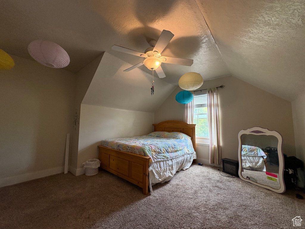 Carpeted bedroom featuring vaulted ceiling, a textured ceiling, and a ceiling fan