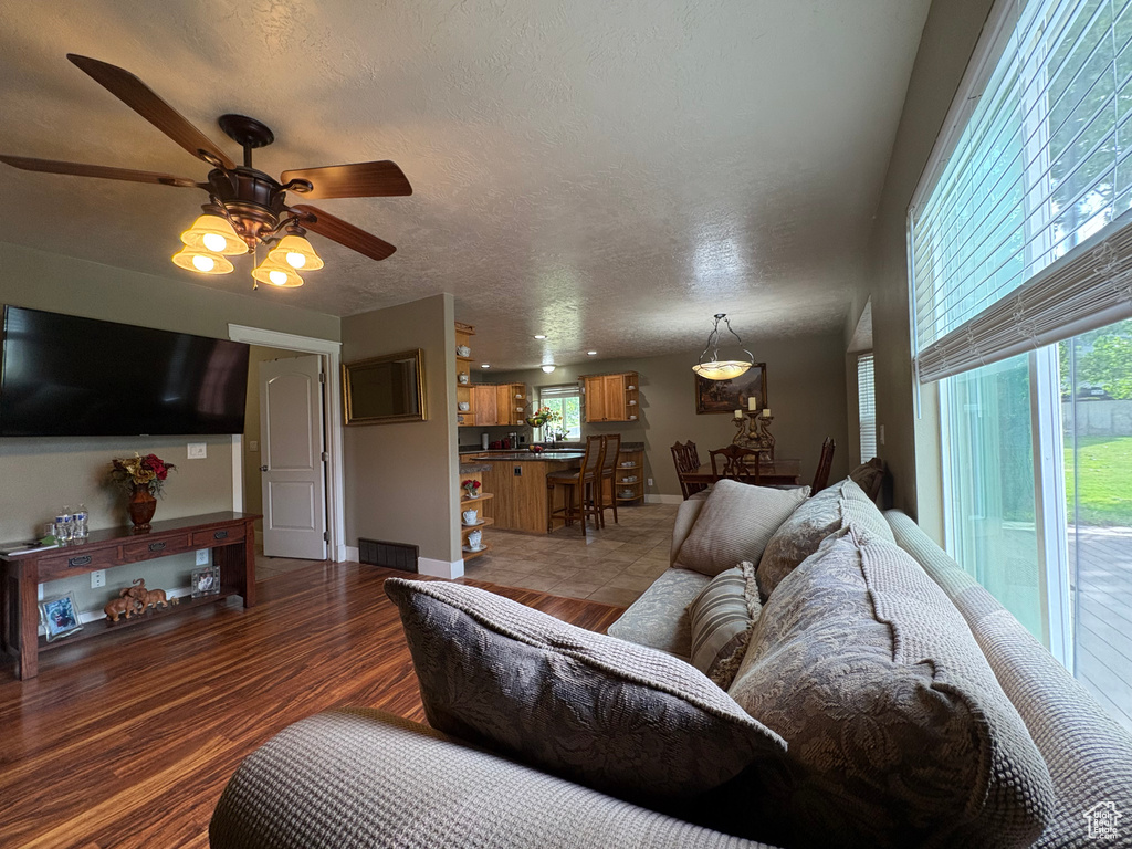 Living room with a ceiling fan, light wood finished floors, and a textured ceiling