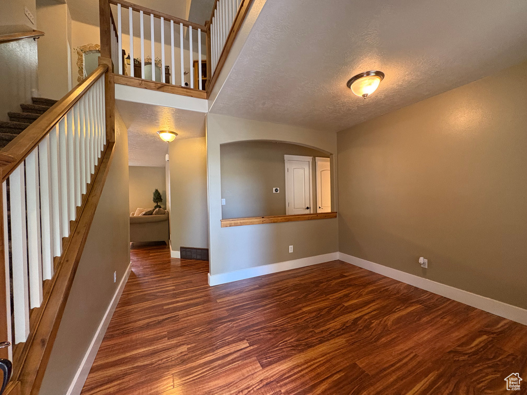Unfurnished living room with wood finished floors, a textured ceiling, stairs, and arched walkways