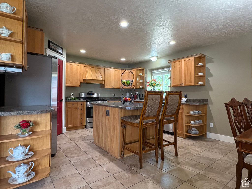 Kitchen with open shelves, appliances with stainless steel finishes, a textured ceiling, recessed lighting, and a breakfast bar area