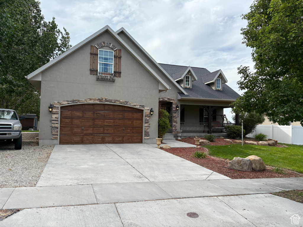 View of front of home with covered porch, stone siding, driveway, and stucco siding