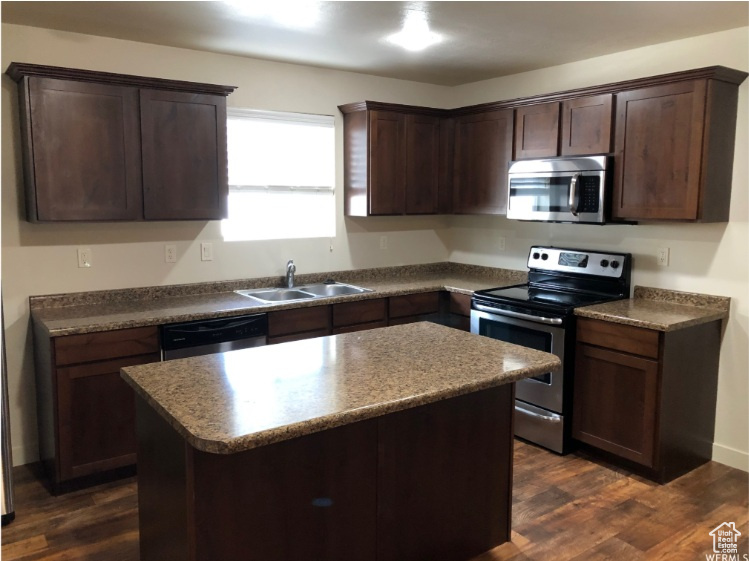 Kitchen with appliances with stainless steel finishes, a kitchen island, dark brown cabinets, and dark wood-style flooring