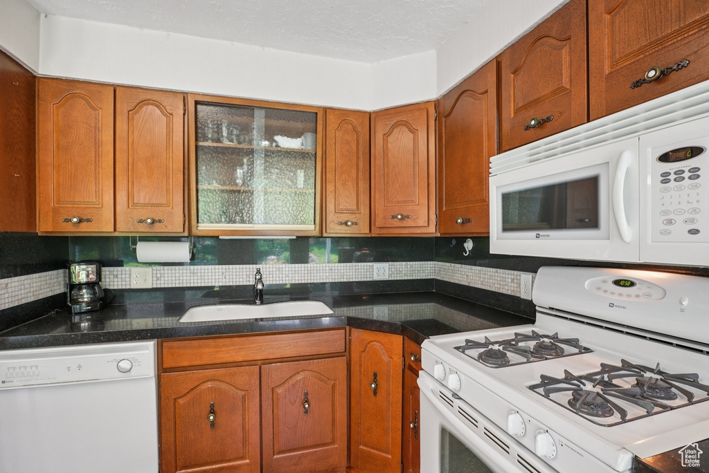 Kitchen with white appliances, brown cabinetry, backsplash, and glass insert cabinets