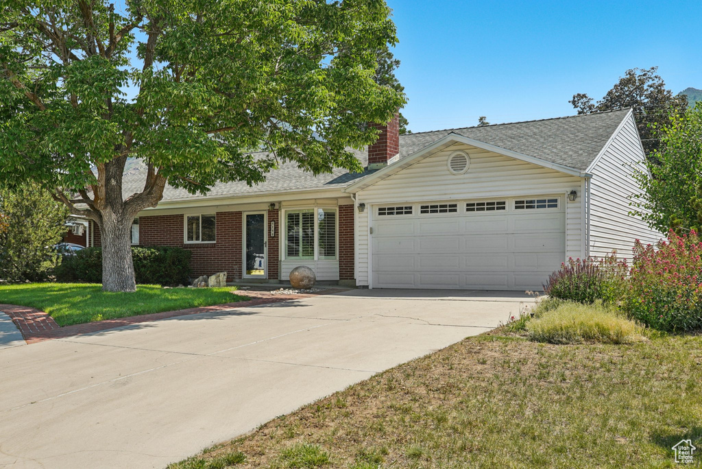 View of front of house with an attached garage, driveway, a chimney, a front yard, and brick siding
