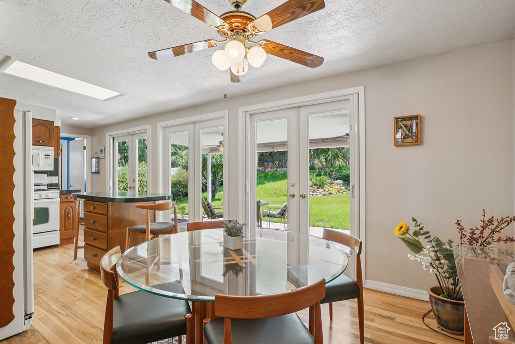 Dining area with french doors, healthy amount of natural light, light wood-style flooring, a textured ceiling, and a skylight