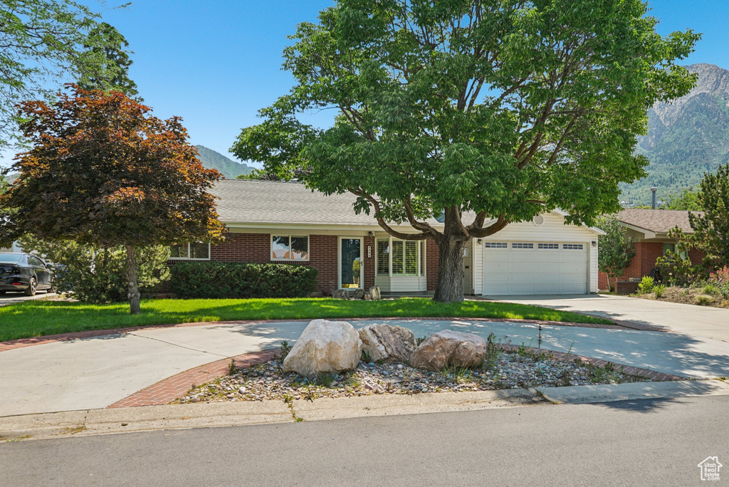 View of front of home with a mountain view, concrete driveway, a front lawn, brick siding, and a garage