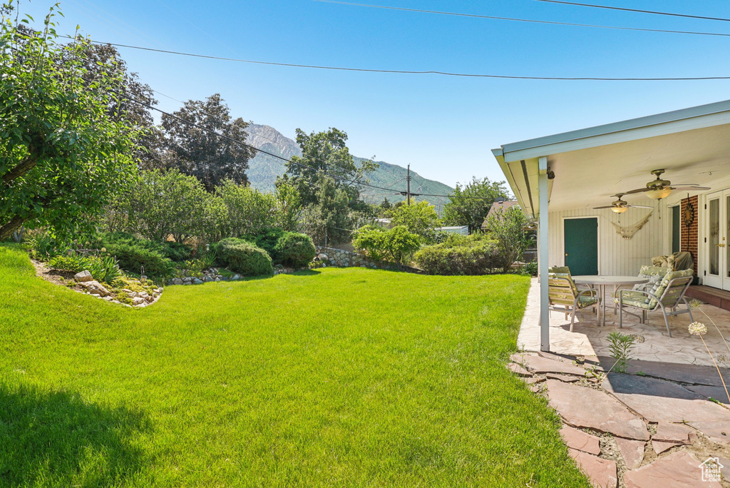 View of green lawn featuring a ceiling fan, a patio, and a mountain view