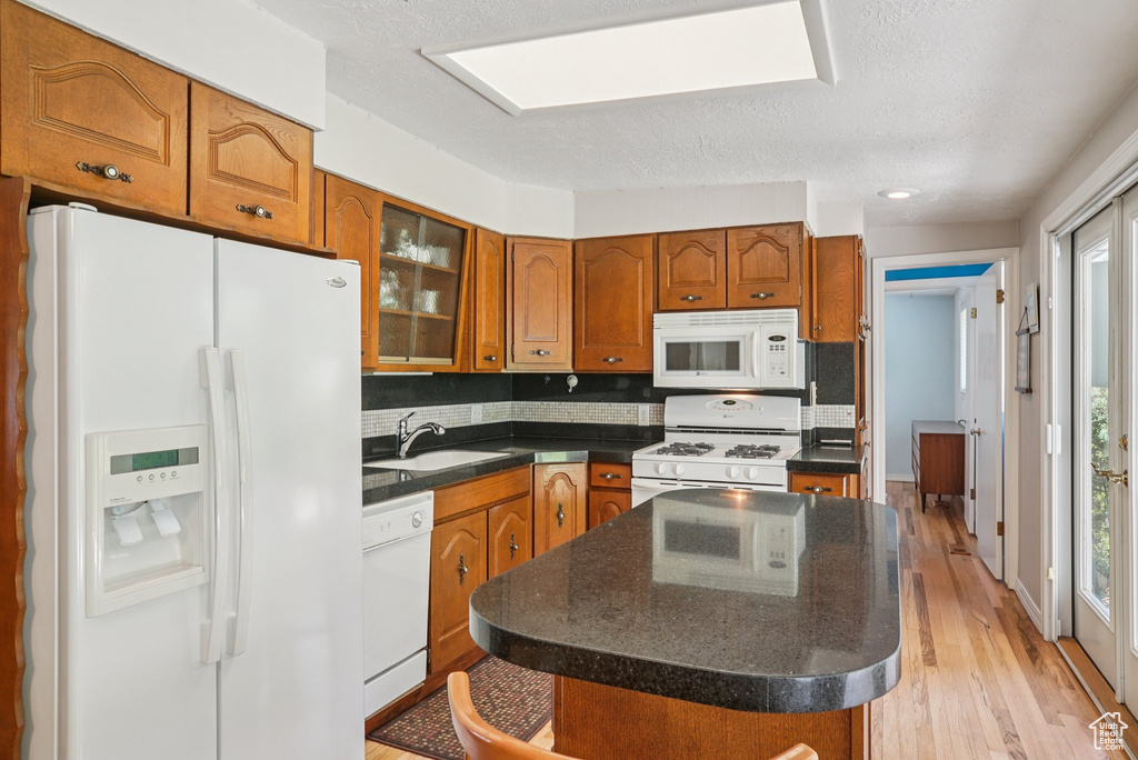 Kitchen featuring white appliances, brown cabinets, backsplash, light wood-type flooring, and a center island