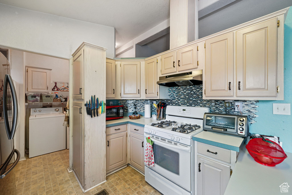 Kitchen with white gas range, under cabinet range hood, washer / clothes dryer, and light countertops
