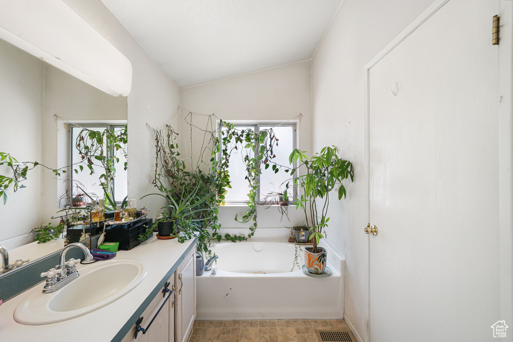 Bathroom featuring vanity, a bath, and lofted ceiling