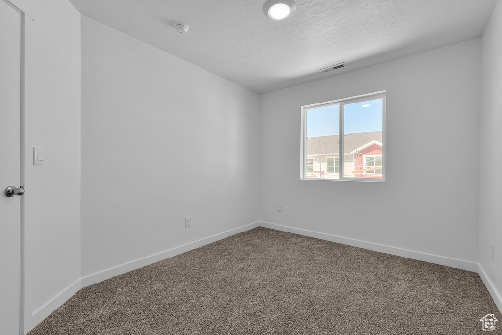 Unfurnished room featuring dark carpet, a smoke detector, and a textured ceiling