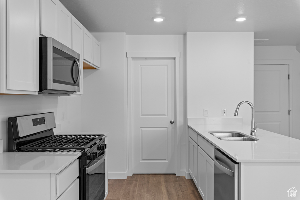 Kitchen with stainless steel appliances, a peninsula, light wood-style floors, light countertops, and white cabinets