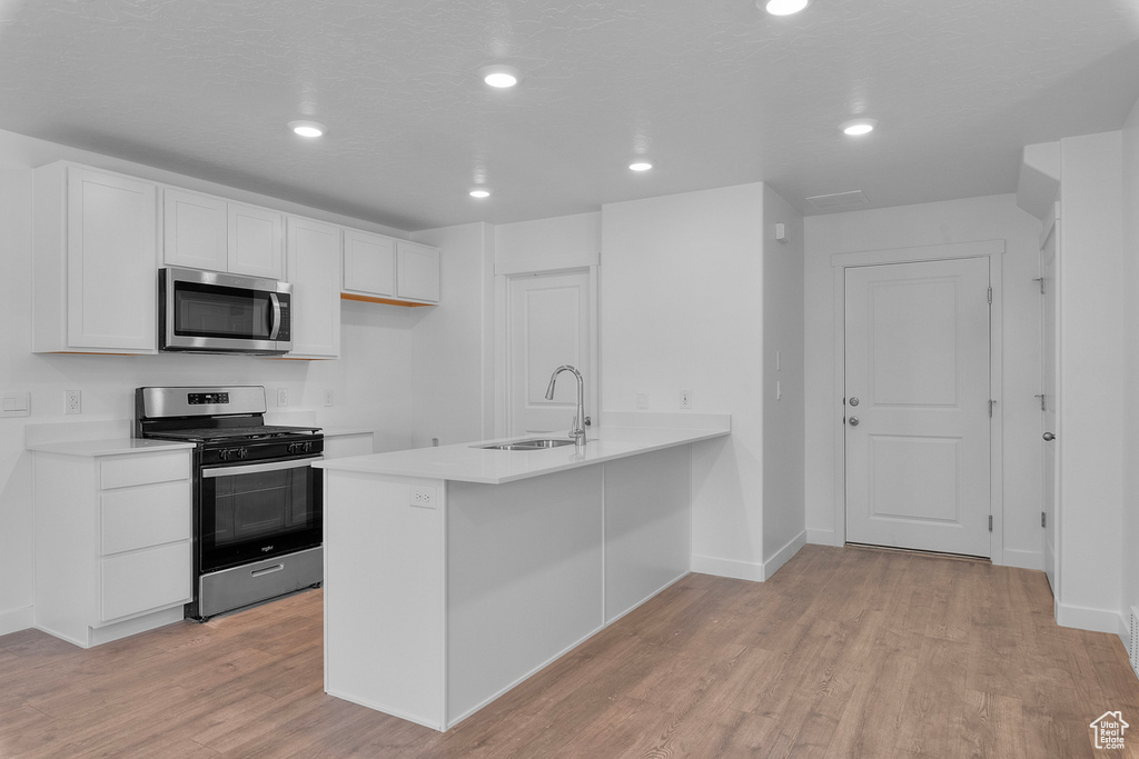 Kitchen featuring stainless steel appliances, white cabinets, light wood-style flooring, light countertops, and recessed lighting