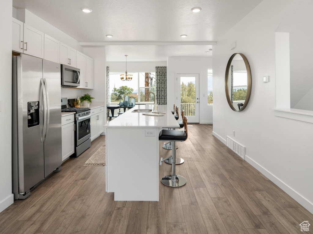 Kitchen with stainless steel appliances, white cabinets, light countertops, a kitchen bar, and an island with sink