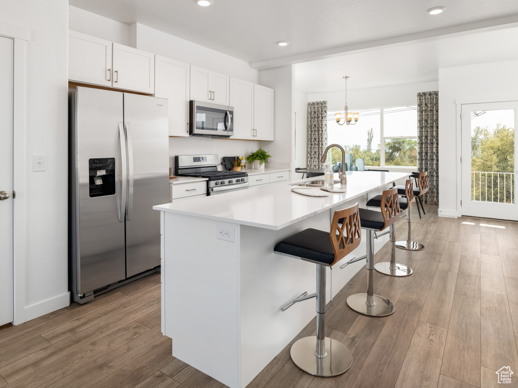Kitchen featuring stainless steel appliances, white cabinets, light wood finished floors, recessed lighting, and a breakfast bar area