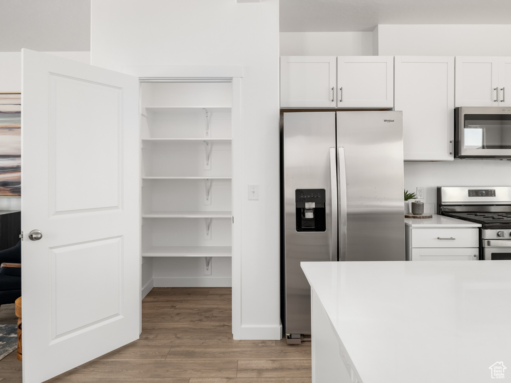 Kitchen with stainless steel appliances, light wood-style flooring, white cabinets, and light countertops