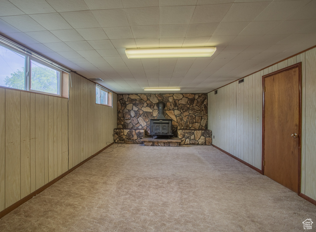 Below grade area featuring carpet flooring, wooden walls, and a wood stove