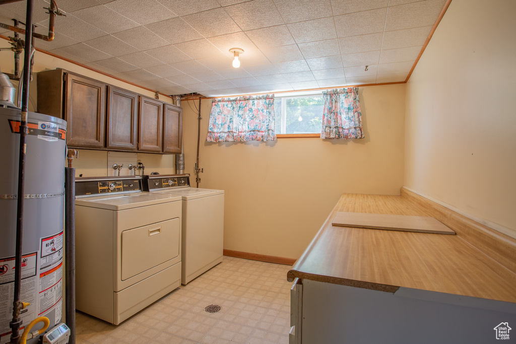 Laundry room with washing machine and clothes dryer, secured water heater, cabinet space, and light flooring