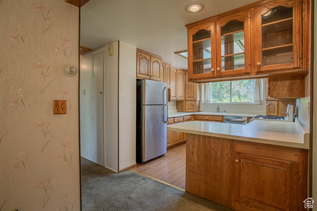 Kitchen featuring appliances with stainless steel finishes, glass insert cabinets, light countertops, light carpet, and a peninsula