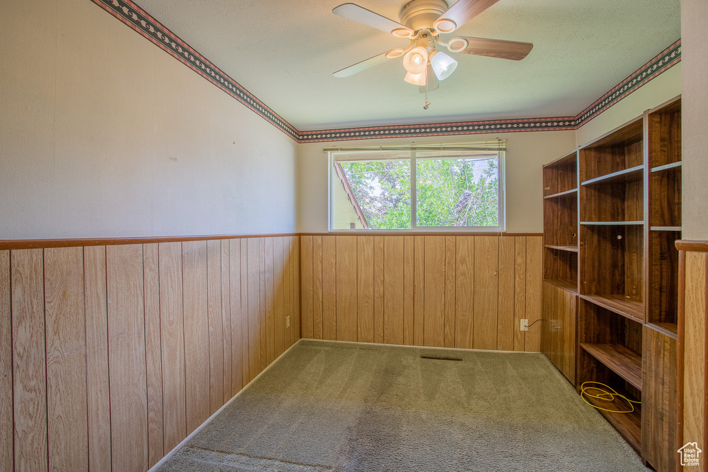 Empty room with wainscoting, wooden walls, a ceiling fan, and carpet floors