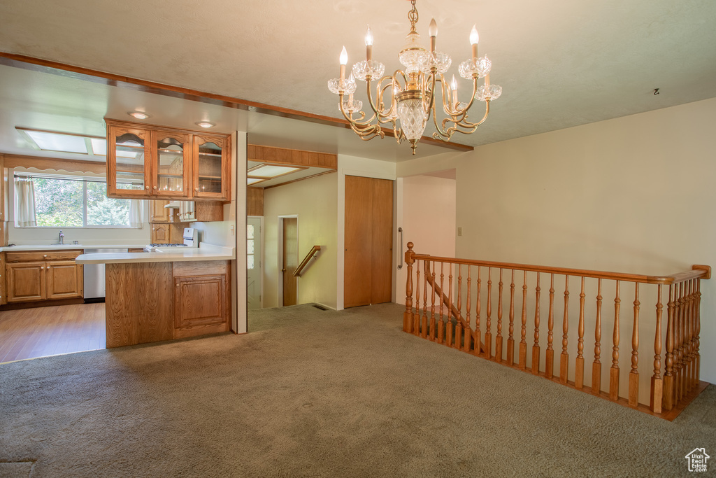 Kitchen with light carpet, glass insert cabinets, light countertops, a chandelier, and brown cabinetry