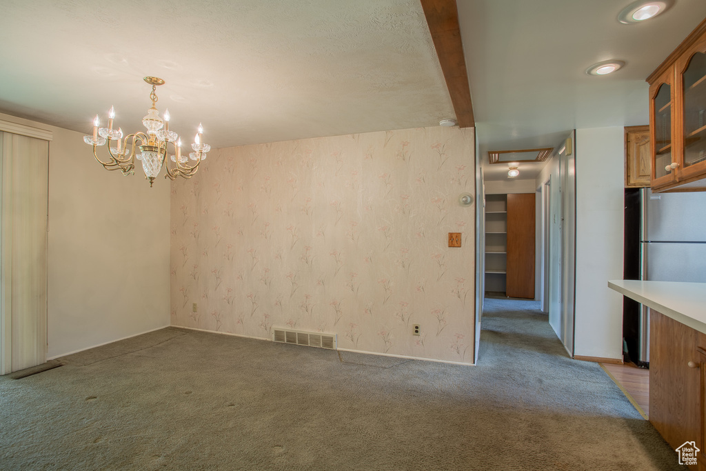 Unfurnished dining area featuring carpet floors, beamed ceiling, and a chandelier