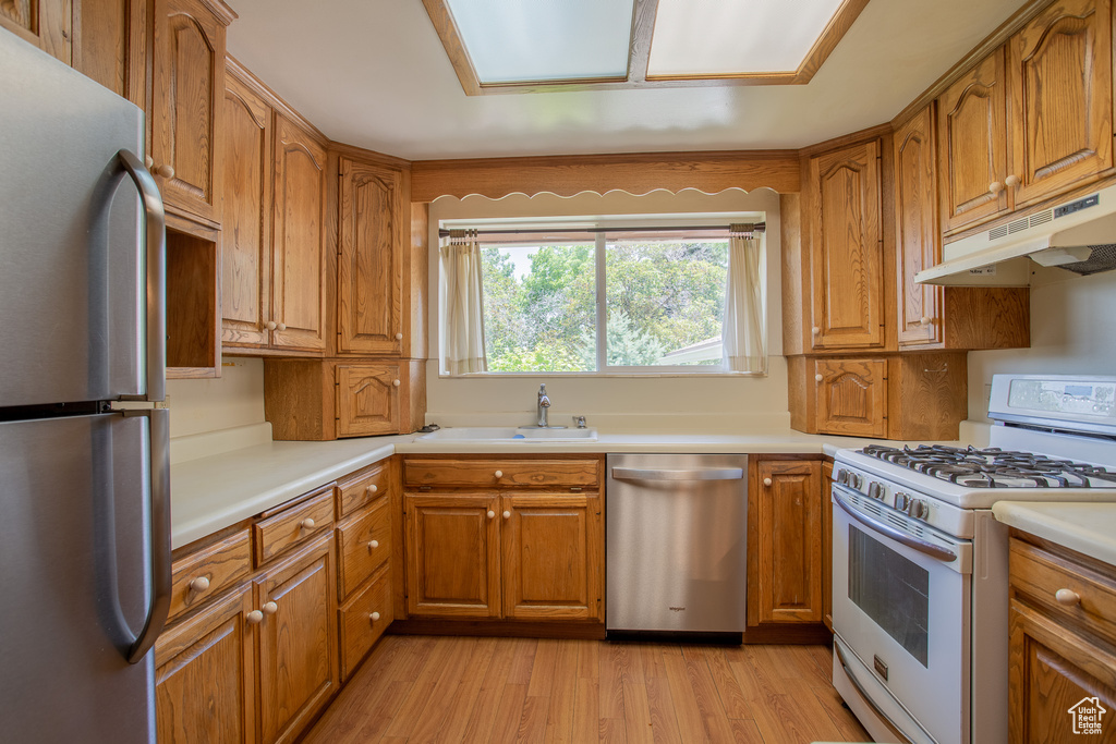 Kitchen with stainless steel appliances, under cabinet range hood, brown cabinets, and light countertops