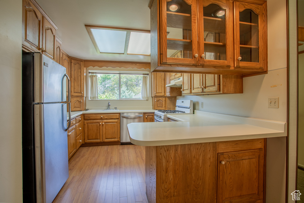 Kitchen featuring stainless steel appliances, under cabinet range hood, a peninsula, glass insert cabinets, and light wood-style floors