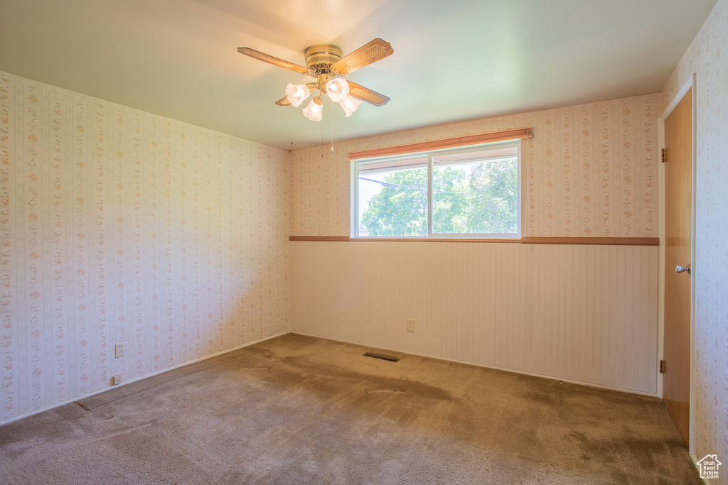 Carpeted empty room with a ceiling fan and wainscoting