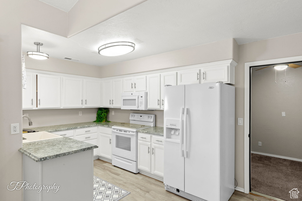 Kitchen featuring white appliances, white cabinets, light countertops, and light wood-style floors