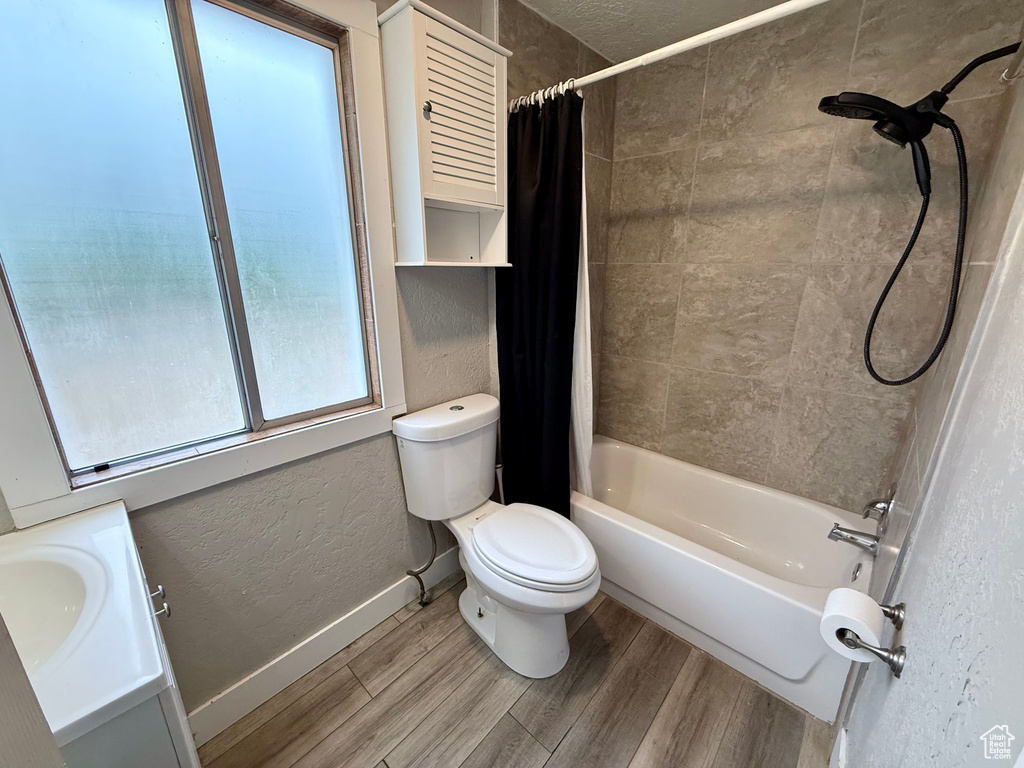 Bathroom with a textured wall, shower / bathtub combination with curtain, wood finished floors, and vanity