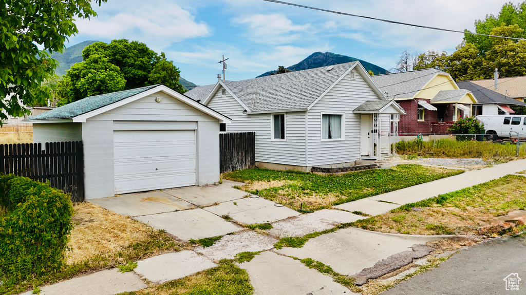 View of front of home featuring driveway, a detached garage, an outdoor structure, a shingled roof, and a mountain view