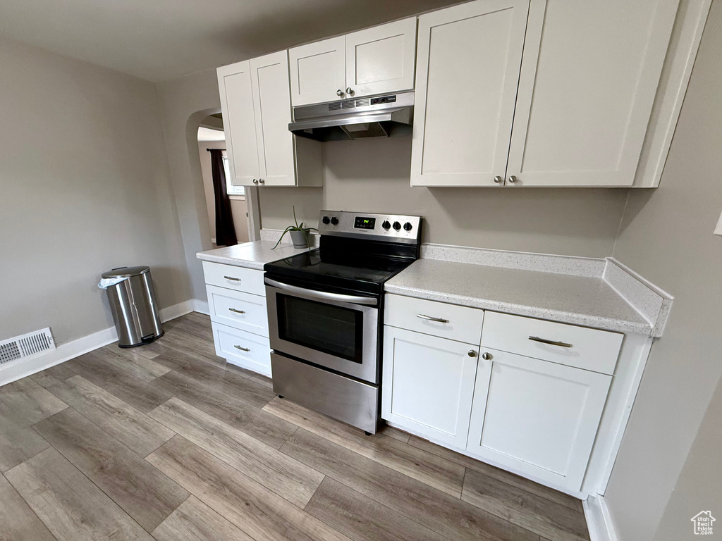 Kitchen featuring stainless steel range with electric stovetop, under cabinet range hood, arched walkways, white cabinetry, and light wood finished floors