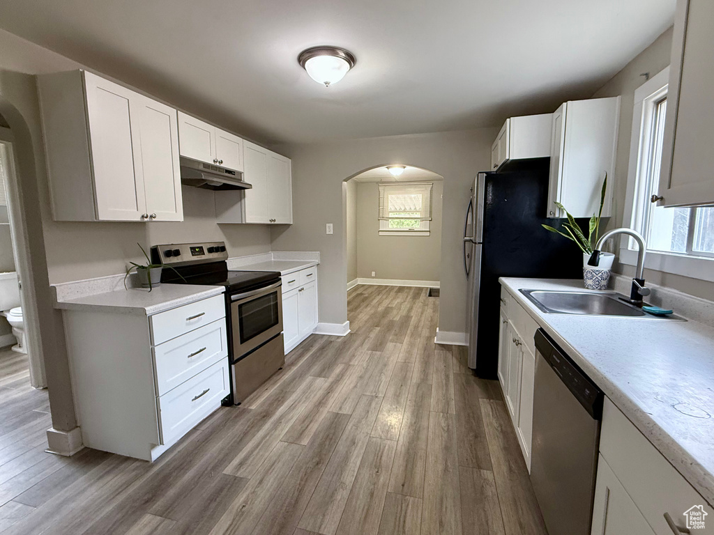 Kitchen featuring stainless steel appliances, arched walkways, under cabinet range hood, light wood-style floors, and light countertops