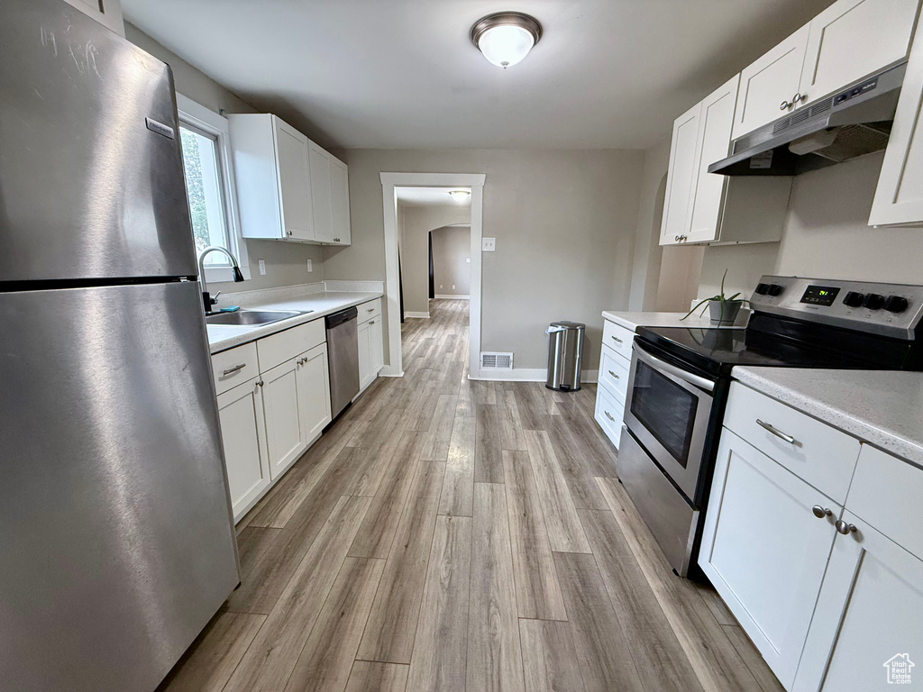 Kitchen featuring stainless steel appliances, under cabinet range hood, light countertops, and white cabinets